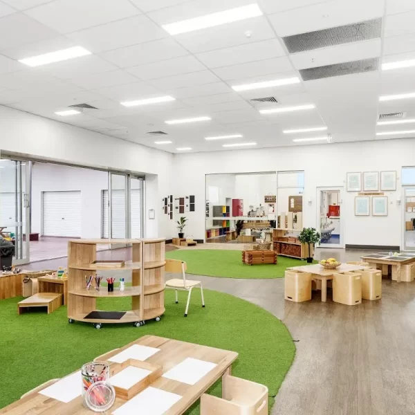 Spacious early learning classroom featuring natural timber furniture, custom storage, open learning zones, indoor-outdoor access, and nature-inspired flooring designed to encourage play and collaboration.
