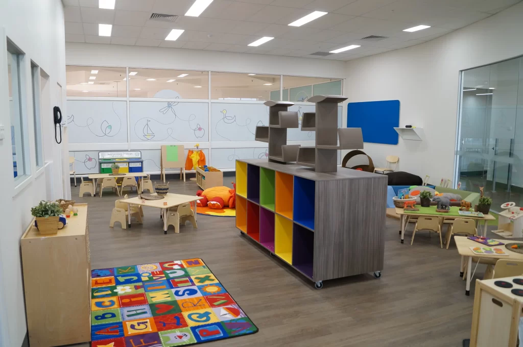 Modern childcare classroom featuring colourful storage units, child-sized furniture, educational play areas, and a bright, open learning environment designed for early childhood education.