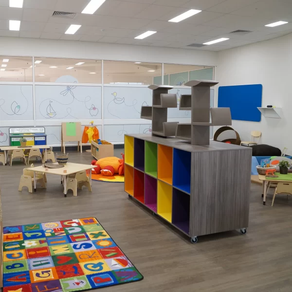 Modern childcare classroom featuring colourful storage units, child-sized furniture, educational play areas, and a bright, open learning environment designed for early childhood education.