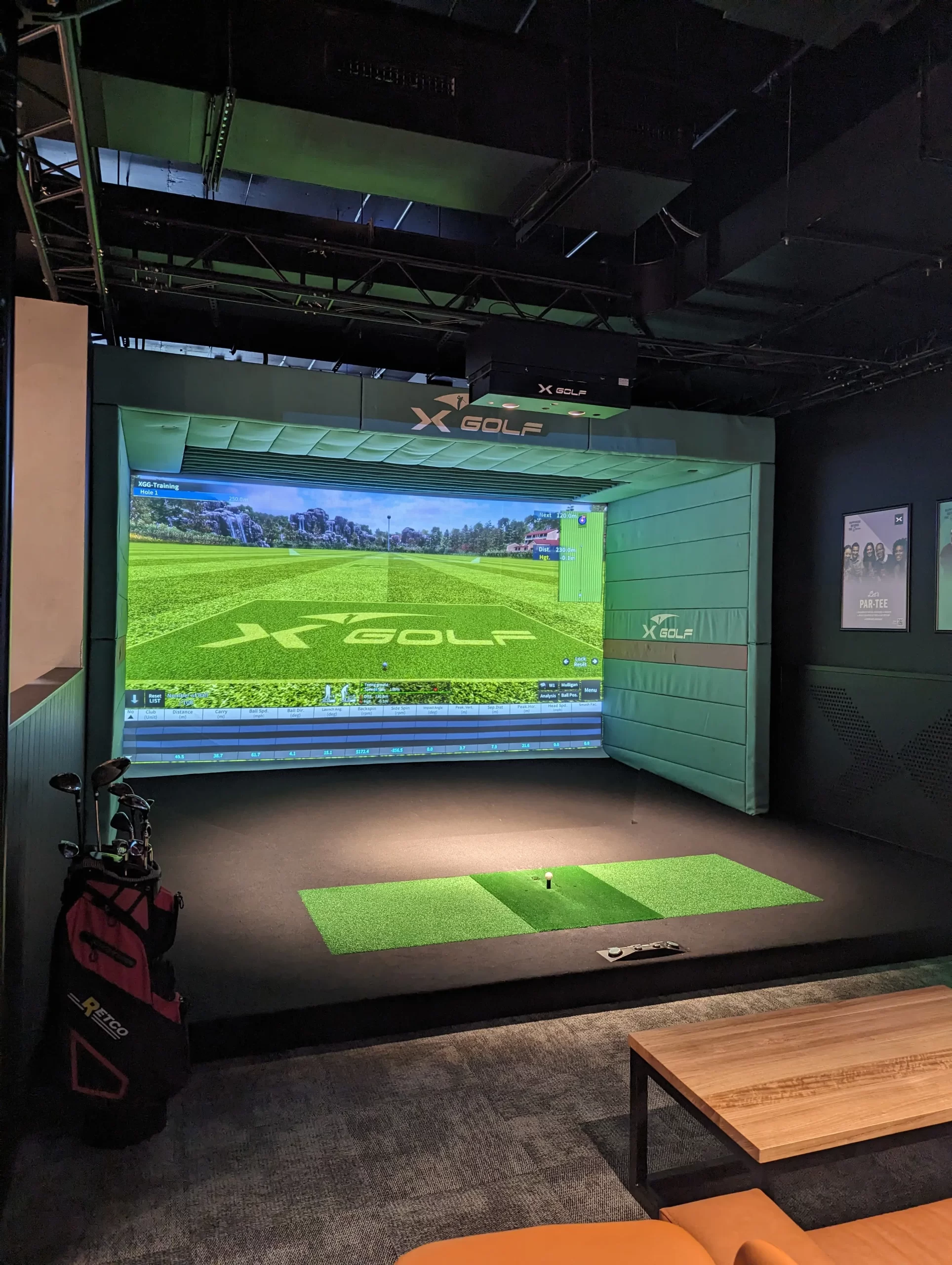 X-Golf indoor golf simulator bay featuring a high-definition projection screen, synthetic turf hitting area, overhead tracking technology, and modern entertainment venue fit-out.