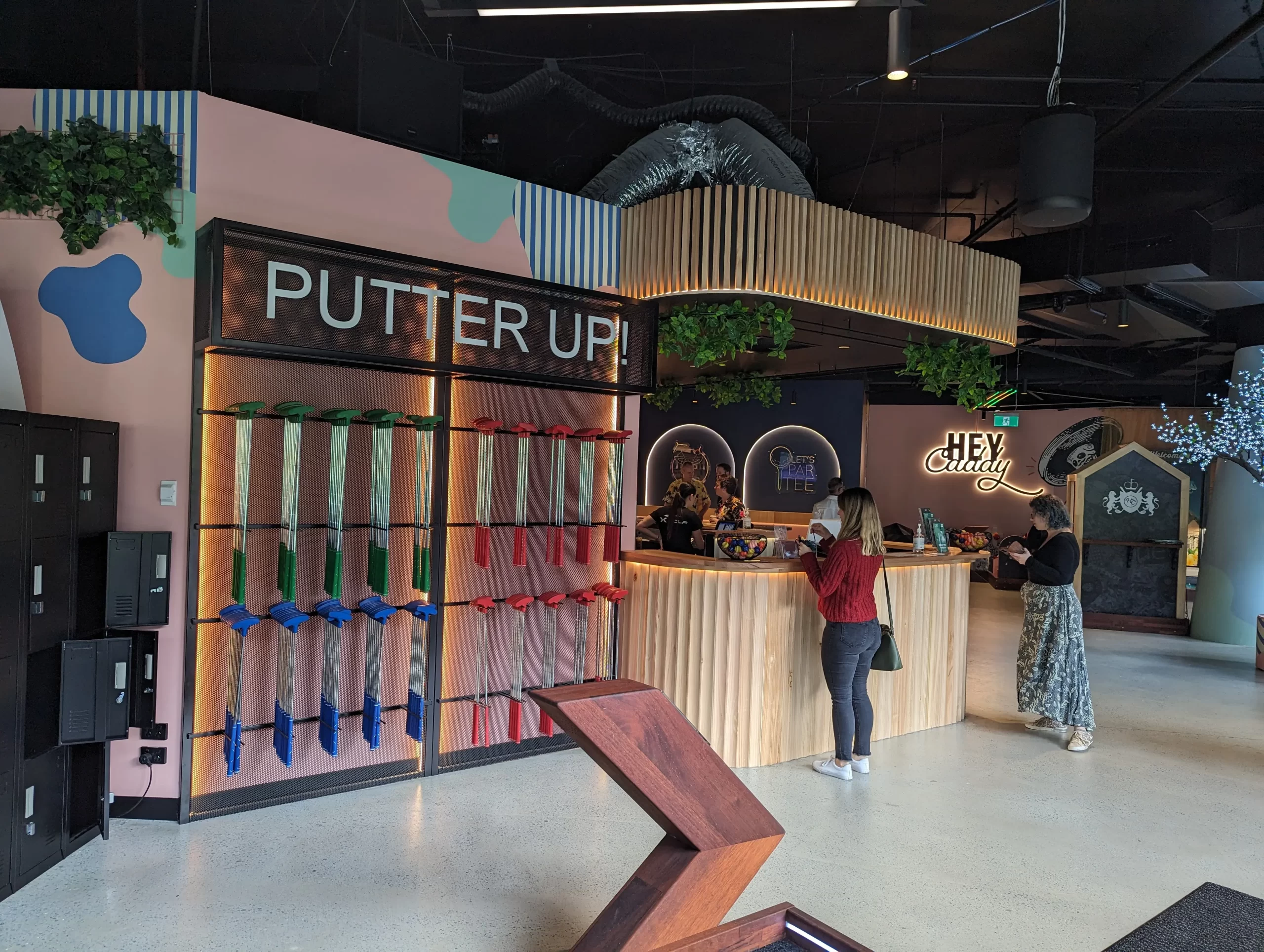 Guests at the X-Golf Southbank mini golf counter beside a putter wall and colourful indoor golf course.