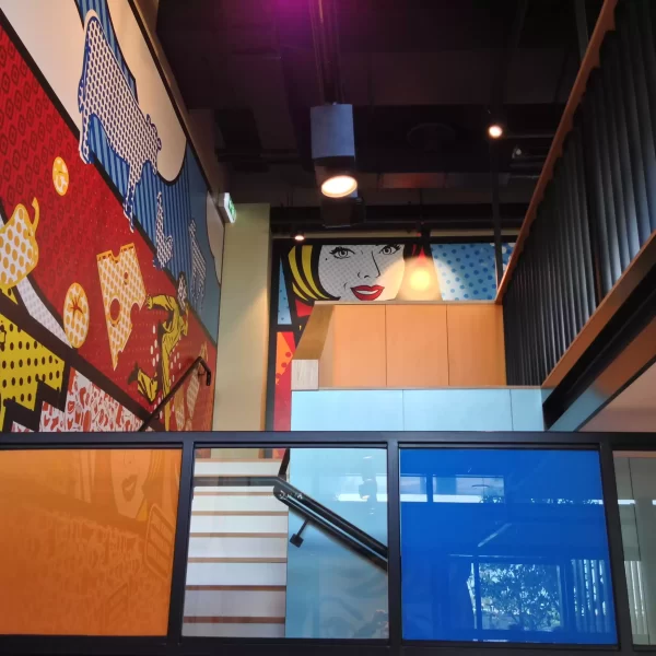 Contemporary interior stairwell featuring vibrant pop-art murals, timber cabinetry, black framing and colourful glass panels.