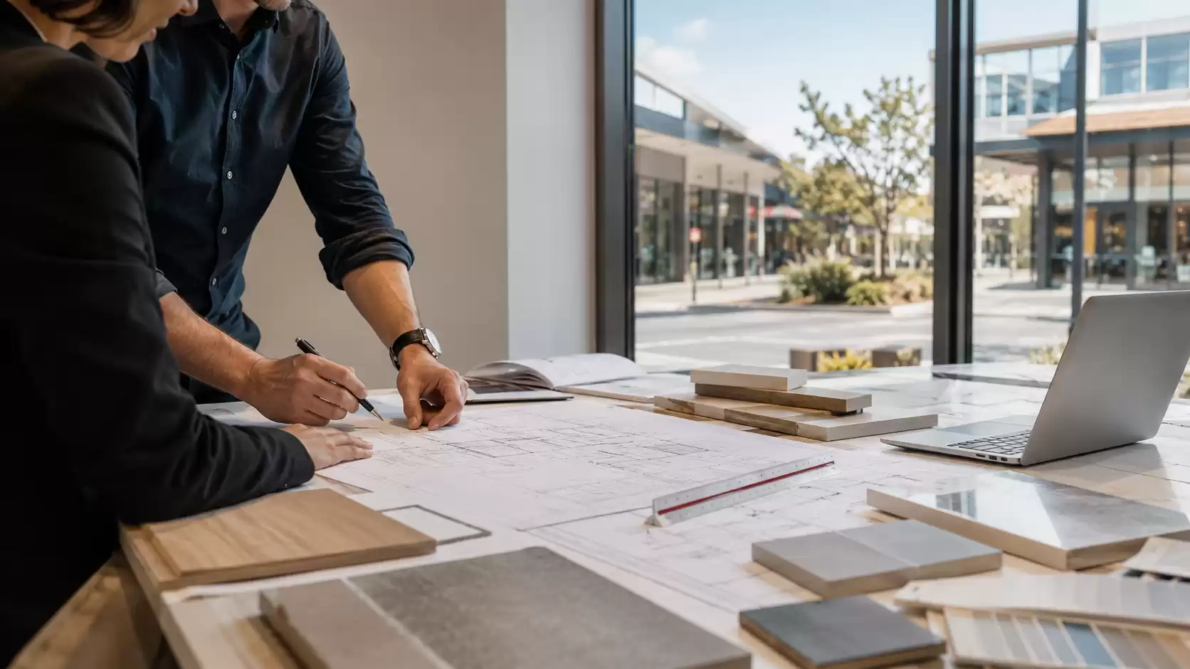 Design professionals reviewing architectural plans, material samples, and layout drawings during a commercial fit-out planning meeting in a modern office.