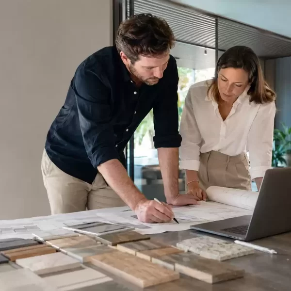 Interior designers reviewing architectural plans and material samples beside a laptop during a commercial fit-out planning meeting.